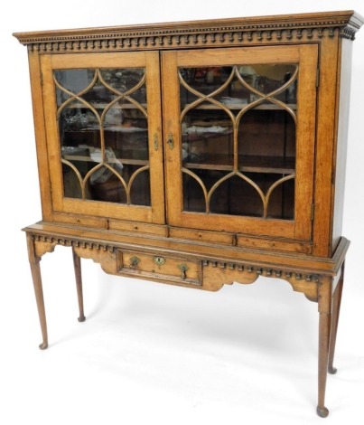 A 19thC oak cabinet bookcase, the drop design top above two astragal glazed doors on sideboard base with single drawer on splayed legs, 163cm high, 156cm wide, 42cm deep.