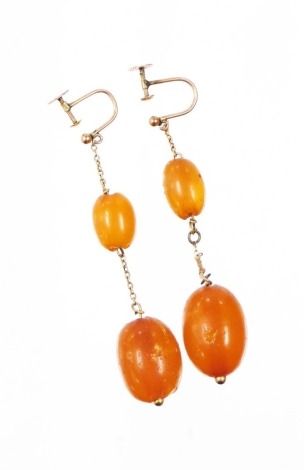 A pair of amber drop earrings, each with a large and small amber bead, 1cm and 2cm, on a yellow metal chain with yellow metal screw in backs, stamped 9ct, 8g all in. (AF)