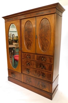 An Edwardian mahogany boxwood strung and satinwood cross banded compactum wardrobe, with top with a moulded and Greek key inlay, above an arrangement of two doors with oval panels enclosing a vacant interior, above two short and three long drawers, flanke