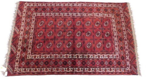 A Bokhara rug, with a typical design of three rows of medallions on a red ground, with multiple borders, 220cm x 140cm.