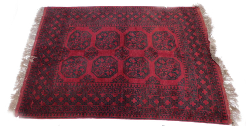 An Afghan rug, with an all over design of medallions, etc., in navy, on a red ground.