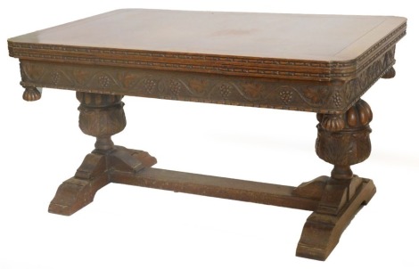 An early to mid 20thC oak draw leaf refectory table, the rectangular top with rounded corners above a frieze carved with grapes and vines, on cup and cover end supports, with flat stretcher, 75cm high, 90cm wide, 220cm long overall.