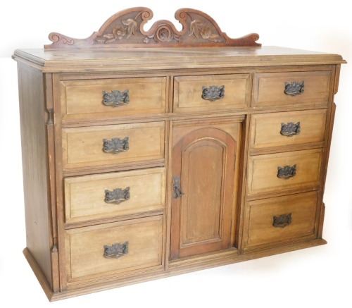 A late Victorian walnut dresser, with a raised back above a moulded edge and an arrangement of nine drawers, each with hammered and ebonised Art Nouveau handles, surrounding a recess with a panel door, 91cm high, 136cm wide.