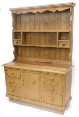 A pine dresser, the associated raised back with various shelves and two drawers, the base with a moulded edge above six drawers and an arched door, on turned feet, 196cm high, 137cm wide.