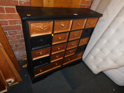 A black and gold painted bank of drawers, with Egyptian style carving.