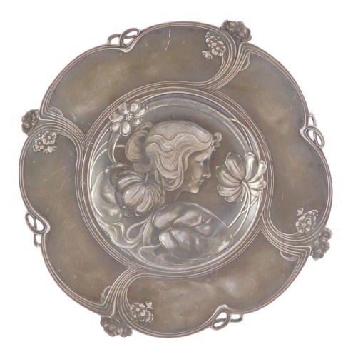 An Art Nouveau late 19thC pewter circular dish, pierced and embossed with a bust portrait of a lady, flowers and sinuous scrolls, 32cm diameter.