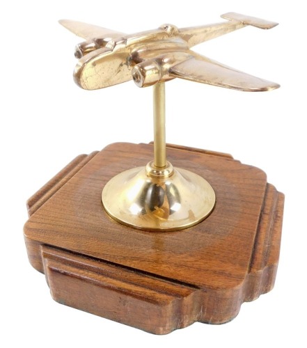 A brass desk stand modelled as a World War II bomber plane, raised on a shaped oak base, 19cm wide.