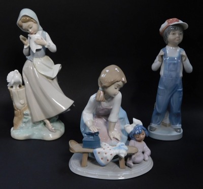 Three Lladro porcelain figures, comprising a kneeling girl with doll and ironing board, standing girls with doves, and a boy in dungarees with an accordian.