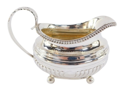 A George III silver cream jug, of semi fluted form, raised on four ball feet, London 1818, 5.10t oz..