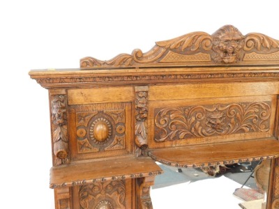 A Victorian oak overmantel mirror, the pediment carved with the head of a lion and foliate scrolls, above a rectangular bevelled glass mirror surmounted and flanked by five shelves with figural or scrolling supports, panels of carved roundels foliate scro - 2