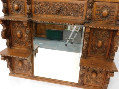 A Victorian oak overmantel mirror, the pediment carved with the head of a lion and foliate scrolls, above a rectangular bevelled glass mirror surmounted and flanked by five shelves with figural or scrolling supports, panels of carved roundels foliate scro - 4