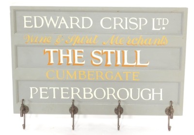 A painted wood and metal wall mounted coat rack, the rectangular panel board painted with "Edward Crisp Ltd Wine and Spirit Merchants, The Still, Cumbergate, Peterborough", the four coat hooks formed as taps, 71.5cm high, 101cm wide.