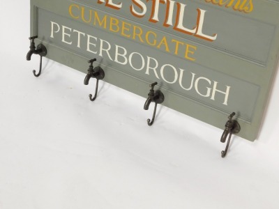 A painted wood and metal wall mounted coat rack, the rectangular panel board painted with "Edward Crisp Ltd Wine and Spirit Merchants, The Still, Cumbergate, Peterborough", the four coat hooks formed as taps, 71.5cm high, 101cm wide. - 2