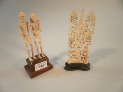 A carved ivory figure of an emaciated man and woman on a wooden plinth