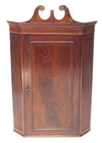 A Georgian style mahogany and boxwood line inlaid hanging corner cupboard, early 20thC, the broken neck pediment, above dentil moulding over a paneled door, opening to reveal three shaped shelves, flanked by channeled sides, 125cm high, 81cm wide, 48cm de