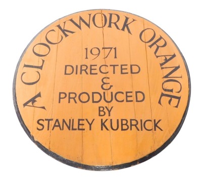 A painted circular wooden table top or wall plaque, painted with "A Clockwork Orange 1971, directed and produced by Stanley Kubrick", black on an orange ground, 60cm diameter.