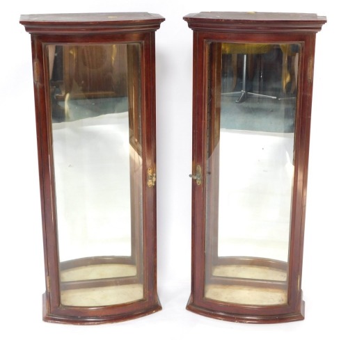 A pair of Victorian mahogany bow front shop display cabinets, with glass panelled sides and door, mirrored back, raised on plinth bases, no shelves, 92cm high, 39.5cm wide, 52cm deep.