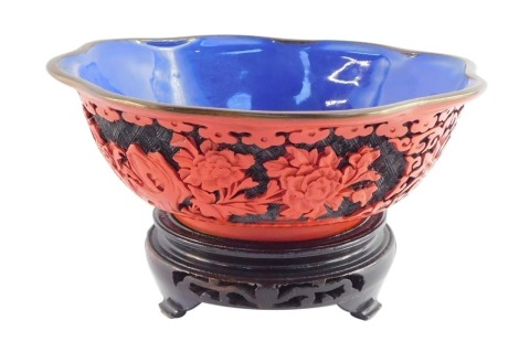 A Chinese Republic cinnabar lacquer bowl, of lobed form with a blue interior, carved to the exterior with flowers and scrolls, raised on a wooden stand, 20cm diameter.