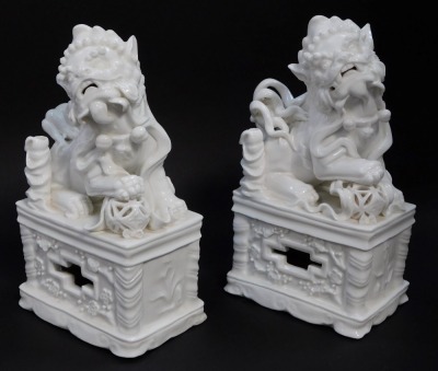 A pair of Chinese Blanc de Chine porcelain figures of Dogs of Fo, modelled with their hands on balls, on plinth bases, 20.5cm high.