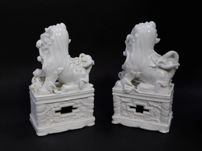 A pair of Chinese Blanc de Chine porcelain figures of Dogs of Fo, modelled with their hands on balls, on plinth bases, 20.5cm high. - 2
