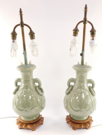 A pair of Chinese Republic celadon porcelain vases, converted to table lamps, of twin handled baluster form, relief decorated with flowers and foliate scrolls, raised on wooden bases, with shades, 64cm high.