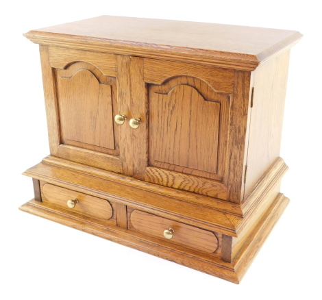 An oak jewellery chest, the out swept pediment over a pair of doors inset internally with mirrors, opening to reveal seven recesses, four long and four short drawers, over two further drawers, raised on a plinth base, 29cm high, 38cm wide, 24cm deep.