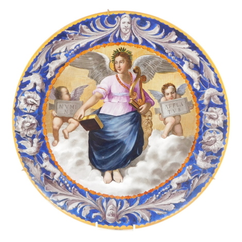 An Italian late 19thC maiolica charger, painted with an angel seated in heaven holding a lyre and a book, flanked by a paid of cherubs holding Latin inscriptions, within a border of masks, birds hunting dogs and flowers, 45cm diameter.