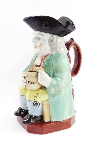 A pearlware early 19thC toby jug, modelled seated holding a jug of frothing stout, 23cm high.