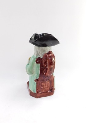 A pearlware early 19thC toby jug, modelled seated holding a jug of frothing stout, 23cm high. - 2