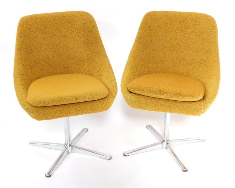 A pair of mid century metal framed swivel dining chairs, upholstered in yellow foliate patterned fabric.