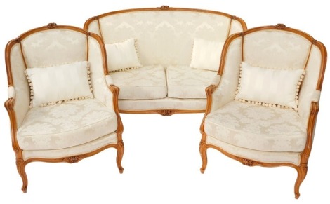 A French Louis XVI style beech wood two seater canape, with a carved show frame, pale gold fabric, floral patterned overstuffed back and loose cushion seats, raised on cabriole legs, 139cm wide, together with a pair of matching fauteuil. (3)