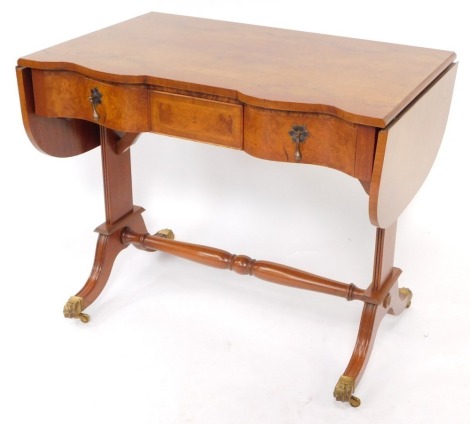 A Georgian reproduction burr walnut and mahogany serpentine fronted sofa table, with a central cushion drawer, flanked by two further drawers, raised on fluted end supports, on out swept feet, brass paw capped on castors, 76cm high, 93cm wide, 148.5cm ext