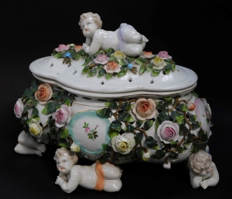 A Sitzendorf early 20thC porcelain casket and cover, of quatre lobed form, encrusted with roses, and with painted floral reserves, finial and four feet moulded as recumbent putti, 26cm wide.