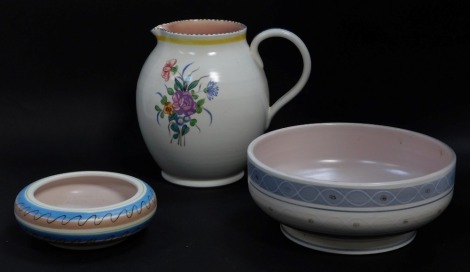 A Poole pottery water jug, traditionally painted with flowers, impressed marks, 19cm high, together with a bowl decorated with banded decoration, printed mark, 22cm diameter, and a similar smaller bowl, 14.5cm diameter. (3)