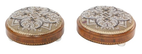 A pair of Victorian walnut and inlaid footstools, with bead worked decorated tops, raised on three porcelain feet, both 31cm diameter.