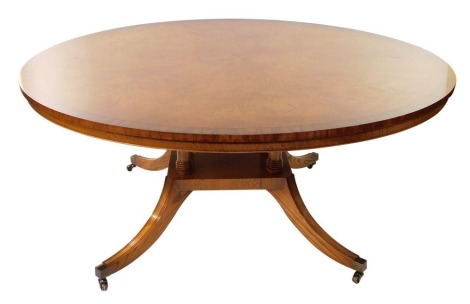 A Bevan & Funnel Limited burr oak circular dining table, raised on four turned column supports above an under tier over four out swept legs, brass caps on casters, 70cm high, 182cm diameter.