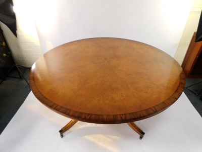 A Bevan & Funnel Limited burr oak circular dining table, raised on four turned column supports above an under tier over four out swept legs, brass caps on casters, 70cm high, 182cm diameter. - 2