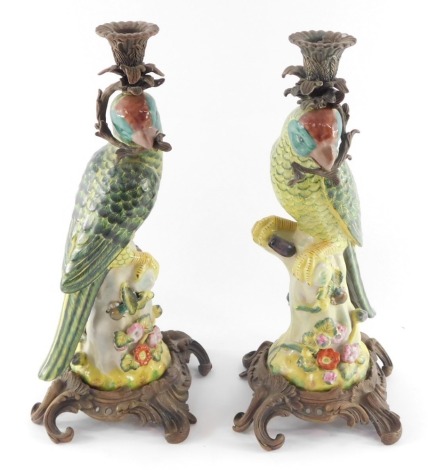 A pair of Meissen style porcelain and metal figural candlesticks modelled as parrots, perched on tree stumps, encrusted with flowers, raised on rococo scroll bases 37.5cm high.