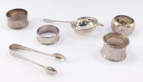 A Victorian silver napkin ring, engraved Geoffrey 1893, Birmingham 1890, three further napkin rings, a George V silver tea strainer and a pair of sugar tongs, Sheffield 1928, 4.6toz.