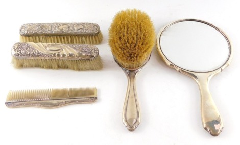 A George V silver backed hand mirror and clothes brush, Birmingham 1921, two silver backed clothes brushes, embossed with flowers and scrolling leaves, and a silver mounted comb, Birmingham 1926.