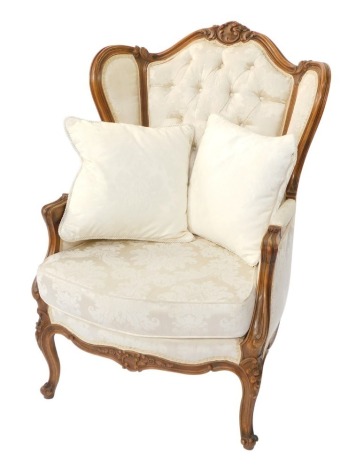 A French 16thC style pale beech wingback fauteuil, upholstered in pale gold floral button back fabric, with loose cushion seat, raised on carved cabriole legs.