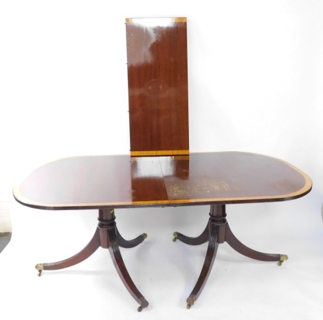 A Georgian style mahogany and yew wood cross banded twin pedestal dining table, with one additional leaf, the columns raised on channelled out swept legs, brass capped on castors, 73.5cm high, 188cm wide, 235cm extended, 107cm deep.