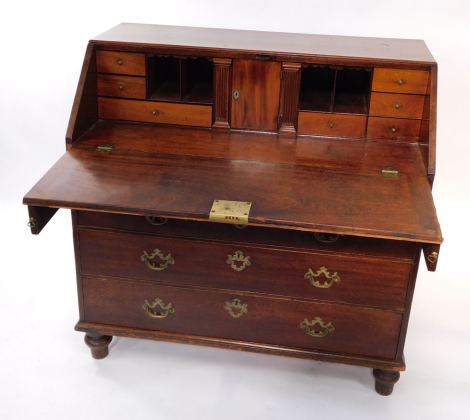 A George III mahogany bureau, the fall flap opening to reveal a central door, flanked by semi secret fluted column compartments, one long medium and five short drawers and four recesses, above two short over three long graduated drawers, raised on turned 