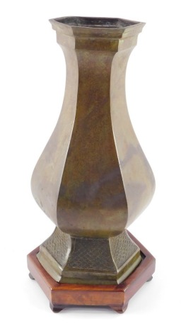 A Chinese bronze vase of hexagonal baluster form, raised on a wooden stand, 38.5cm high.