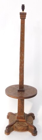 An Anglo Indian early 20thC standard lamp, carved with flowers and leaves, having a square column with a central circular table base, above a circular stand with four out swept stylised feet, 134cm high.