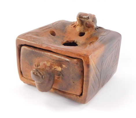 A rustic terracotta ashtray, carved with frogs, the top with holes over an ash drawer, 8.5cm wide.