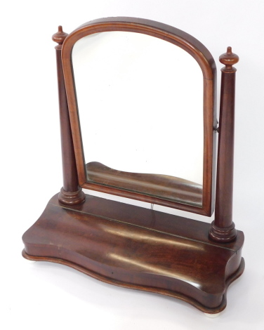 A Victorian mahogany serpentine fronted swing frame toilet mirror, the domed mirror on twin turned supports, over a base with single hinged compartment, raised on porcelain and wooden bun feet, 84cm high, 73cm wide.