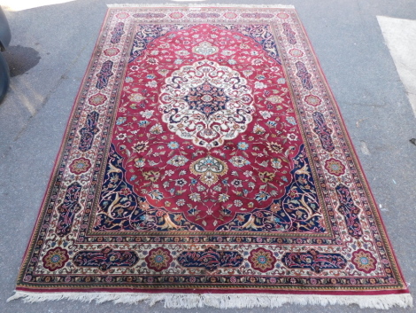 An Isfahan rug, with red and blue ground, decorated with a central floral medallion within interlaced floral motifs, within repeating floral and geometric borders, signed, 339cm x 225cm.