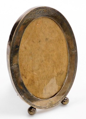 A sterling silver photograph frame, with bright cut decoration and initialled 'RWB', on ball feet, oval aperture to show 16.5cm x 11cm, inscribed Jan 23rd 1917 verso, indistinct hallmarks for Birmingham, 21cm high. (lacks back)