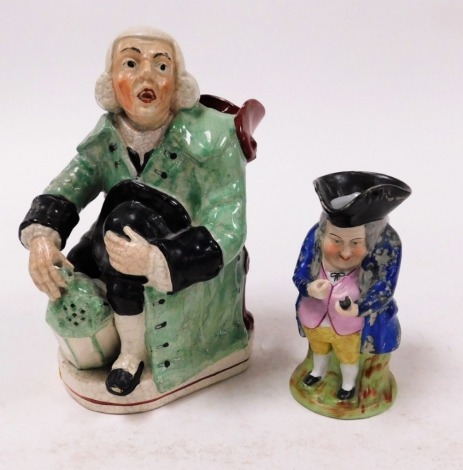 Two Staffordshire character jugs, to include a large Staffordshire potters character jug, of a seated gentleman in green outcoat, 23cm high, and another porcelain character jug, 15cm high. (2)